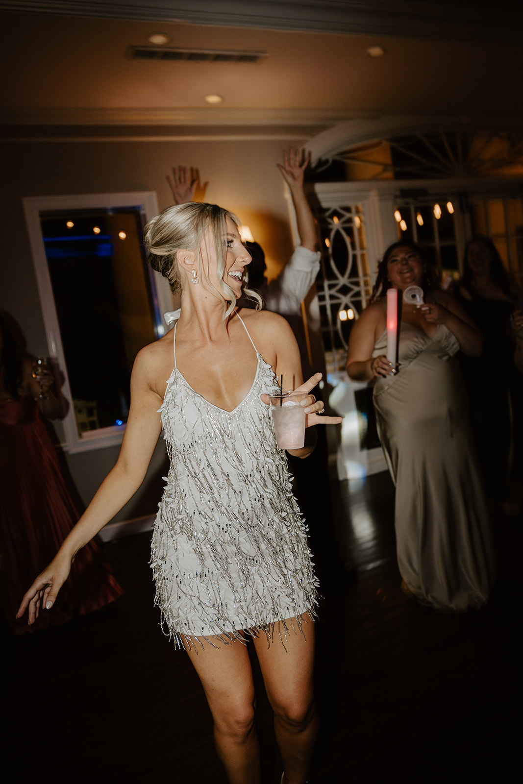 Bride dances enthusiastically in a sparkly fringe dress, holding a cocktail at the reception after-party.